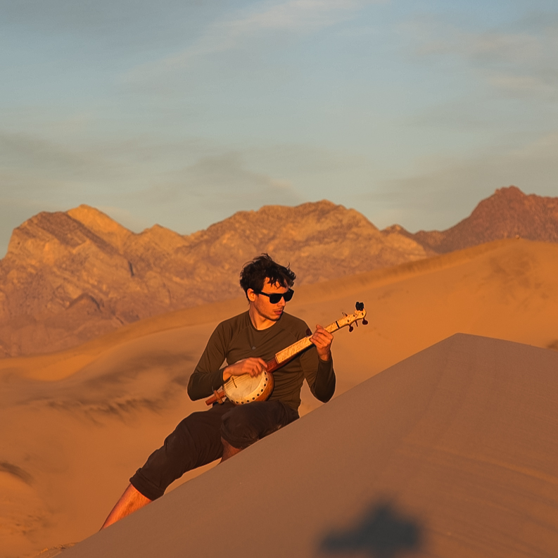man on sand dunes playing a gourd banjo